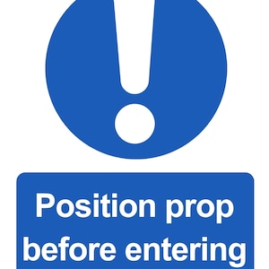 May include: A blue and white safety sign with an exclamation point inside a blue circle above a blue rectangle. The rectangle contains the white text: "Position prop before entering."