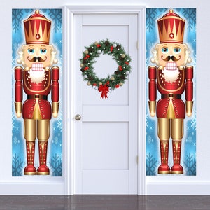 May include: Two tall nutcracker door decorations with red and gold accents, standing on a blue background with snowflakes. A green Christmas wreath with red berries hangs on a white door.