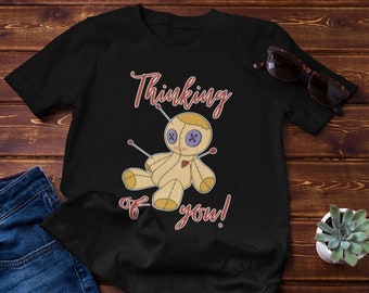 May include: Black t-shirt with a red and white graphic of a voodoo doll with the text "Thinking of you!"