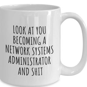 May include: White ceramic mug with a black text that reads: "LOOK AT YOU BECOMING A NETWORK SYSTEMS ADMINISTRATOR AND SHIT". The mug has a curved handle and is designed for hot beverages.