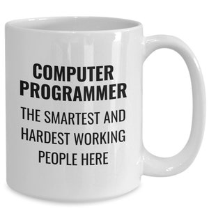 May include: White ceramic mug with the text "COMPUTER PROGRAMMER THE SMARTEST AND HARDEST WORKING PEOPLE HERE" in black, bold font. The mug has a curved handle and a glossy finish.