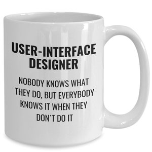 May include: White ceramic mug with the text "USER-INTERFACE DESIGNER" and a humorous quote about the profession. The mug has a curved handle and is suitable for hot or cold beverages.