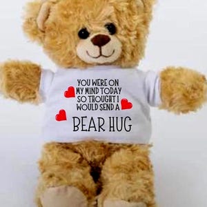 May include: A plush teddy bear with light brown fur and a white t-shirt. The shirt has the text "YOU WERE ON MY MIND TODAY SO THOUGHT I WOULD SEND A BEAR HUG" with red heart accents. The bear has black eyes and a brown nose.