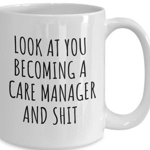 Może przedstawiać: Biały ceramiczny kubek z zakrzywionym uchwytem. Kubek ma czarny tekst z napisem „LOOK AT YOU BECOMING A CARE MANAGER AND SHIT”.