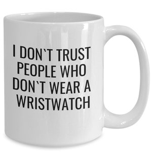 Puede incluir: Taza de cerámica blanca con asa curva. La taza presenta texto negro que dice: "NO CONFÍO EN LA GENTE QUE NO USA RELOJ DE PULSERA."