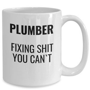 May include: White ceramic mug with the words "PLUMBER FIXING SHIT YOU CAN'T" printed in black. The mug has a curved handle and a glossy finish, suitable for hot beverages.