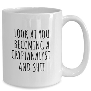 May include: White ceramic coffee mug with a curved handle. The mug features black text that reads: "LOOK AT YOU BECOMING A CRYPTANALYST AND SHIT."