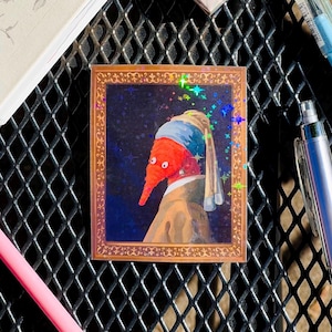 May include: A sticker featuring a red worm with a blue and white turban and a pearl earring. The worm is depicted in a painting style, with a dark blue background and gold frame. The sticker has a holographic finish with glitter accents.