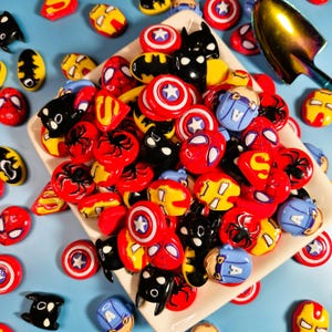 May include: A set of three ceramic mugs with a speckled, cream-colored glaze. Each mug features a different hand-painted design: a blue and green leaf, a yellow flower, and a red berry. The mugs have a simple, rounded shape.