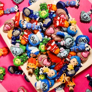 Puede incluir: Una colección de figuritas de personajes coloridos en un tazón blanco. Las figuritas son de diferentes formas y tamaños, y todas llevan diferentes expresiones. Algunas de las figuritas llevan gafas, mientras que otras llevan sombreros. Las figuritas están hechas de plástico y son muy detalladas.