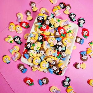 Puede incluir: Una colección de encantos de personajes de princesas de dibujos animados coloridos, con varias princesas en diferentes poses y atuendos. Los encantos están hechos de un material suave y flexible y son perfectos para agregar un toque de fantasía a las manualidades y los proyectos.