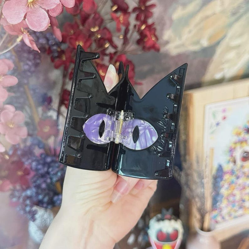 May include: Black claw hair clip with a purple and white marbled eye design. The clip is held open, revealing the inner workings. The clip is a unique hair accessory.