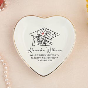 May include: Heart-shaped white ceramic trinket dish with a gold rim. The dish features a graduation cap design with a map, the name "Alexander Williams", and the text "Willow Creek University, Class of 2026".
