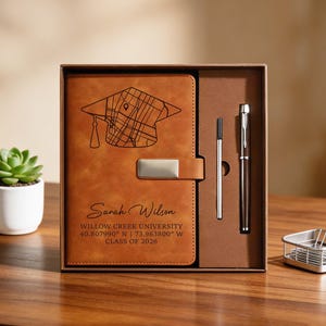 May include: A graduation gift set featuring a brown leather journal with a map and mortarboard design, a pen, and a pencil. The journal is personalized with a name, university, and graduation year. The set is presented in a brown box.