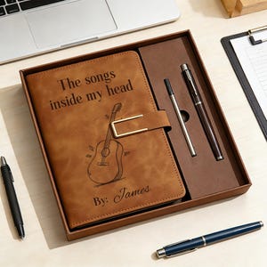 Può includere: Un diario in similpelle marrone in una confezione regalo con chiusura in metallo dorato. La copertina presenta un'illustrazione di chitarra e il testo "The songs inside my head" e "By: James". Il set include una penna marrone e un refill argentato.