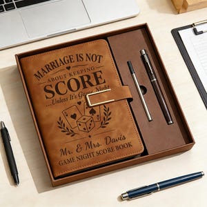 May include: A brown leather-like score book in a gift box with a matching pen and refill. The cover features the text "MARRIAGE IS NOT ABOUT KEEPING SCORE... Unless It's Game Night", "Mr. & Mrs. Davis", and "GAME NIGHT SCORE BOOK" with playing cards and dice.