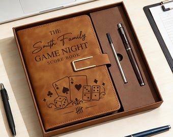 May include: A brown rectangular score book with a gold metal clasp, featuring the text THE Smith Family GAME NIGHT SCORE BOOK and illustrations of playing cards, dice, and dominoes. The book is inside a box with a pen and a metal refill.