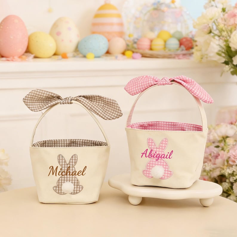 Pu&ograve; includere: Due cestini pasquali color crema con manici a forma di orecchie di coniglio. Un cestino ha un fiocco a quadretti marrone e il nome "Michael". L'altro ha un fiocco a quadretti rosa e il nome "Abigail". Entrambi hanno dettagli di coda di coniglio.