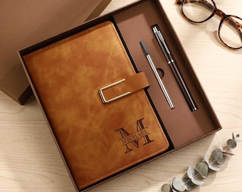 May include: A tan notebook with a gold-toned metal clasp and the name MICHAEL engraved in a large letter M, presented in a brown gift box with a matching pen and a refill cartridge. The set is accompanied by tortoise-shell patterned glasses.