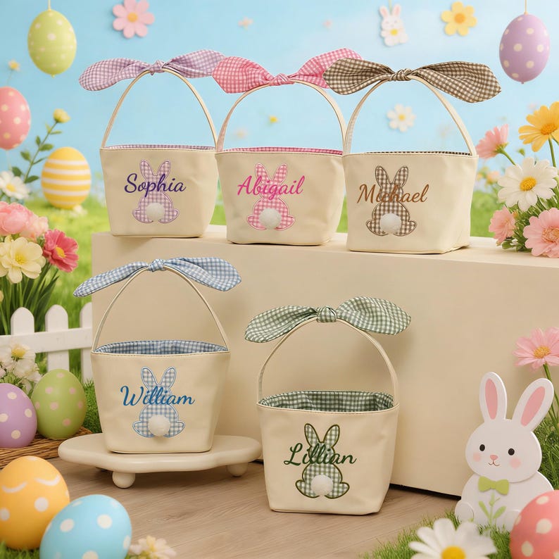 Pu&ograve; includere: Cesti pasquali color crema con manici a fiocco a quadretti. Ogni cesto presenta un design a coniglietto e un nome: Sophia, Abigail, Michael, William e Lillian. Uova di Pasqua e fiori circondano i cesti.