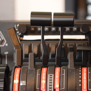 Puede incluir: Primer plano de un panel de control de avión negro con múltiples interruptores y palancas. Las palancas tienen mangos negros y etiquetas rojas que dicen "Retire antes del vuelo".