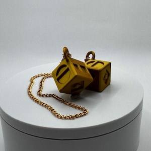 May include: A gold chain necklace with two gold dice pendants. The dice are cube-shaped and have a textured surface.