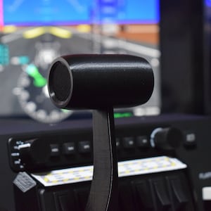 Könnte beinhalten: Nahaufnahme eines schwarzen Flugzeug-Gashebels mit einem strukturierten Knopf. Der Hebel ist an einem schwarzen Panel mit verschiedenen Knöpfen und Bedienelementen befestigt.
