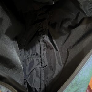 K&ouml;nnte beinhalten: Innenansicht einer schwarzen Tragetasche mit einer kleinen Tasche. Das Futter der Tasche ist schwarz, und die Au&szlig;enseite hat ein schimmerndes, irisierendes Finish mit Blau- und Gr&uuml;nt&ouml;nen. Die Tasche ist offen und zeigt das Innere.