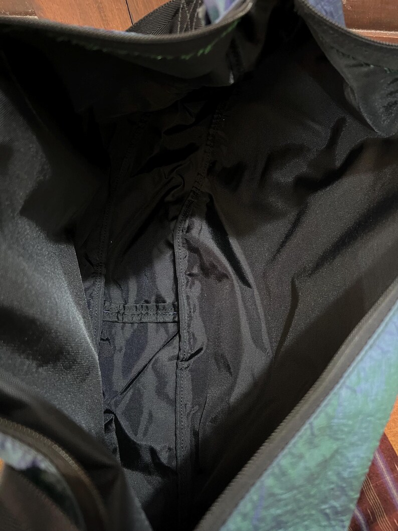 K&ouml;nnte beinhalten: Innenansicht einer schwarzen Tragetasche mit einer kleinen Tasche. Das Futter der Tasche ist schwarz, und die Au&szlig;enseite hat ein schimmerndes, irisierendes Finish mit Blau- und Gr&uuml;nt&ouml;nen. Die Tasche ist offen und zeigt das Innere.