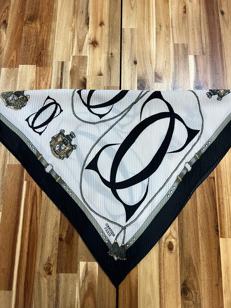 May include: White and black silk scarf with a repeating pattern of interlocking black letter Cs, rope, and decorative elements. The scarf has a black border and the words "CARTIER PARIS".