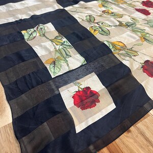 May include: A silk scarf with a patchwork design. The scarf features alternating sections of black and white stripes, and squares with a red rose print. The scarf also has a floral pattern with red roses and green leaves.