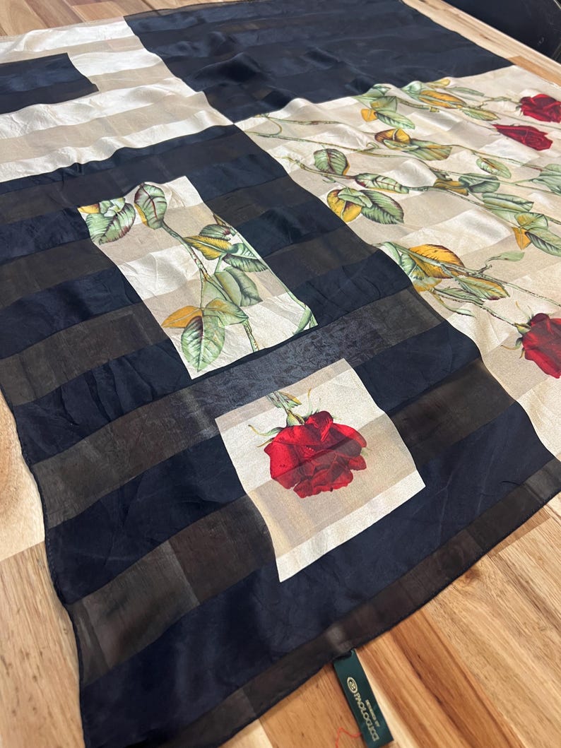May include: A silk scarf with a patchwork design. The scarf features alternating sections of black and white stripes, and squares with a red rose print. The scarf also has a floral pattern with red roses and green leaves.