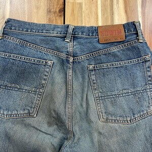 May include: Close-up of the back of blue denim jeans. The jeans have two back pockets and a brown leather patch with the brand name "EDWIN". The jeans are labeled "505X 33 34".