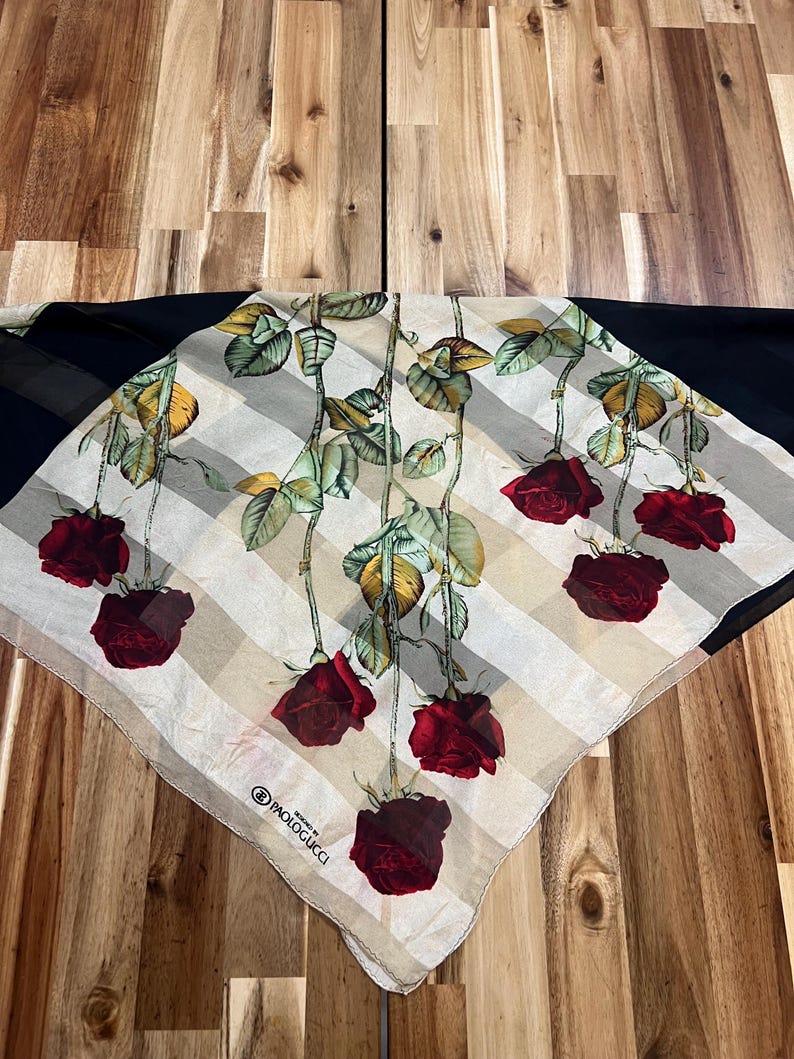May include: A square scarf featuring a floral design of red roses with green leaves and stems. The scarf has a striped pattern in beige and white, with a black border. The brand name "PAOLOGUCCI" is visible.