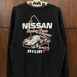 Może przedstawiać: Czarna bluza z białym nadrukiem graficznym przedstawiającym samochód wyścigowy oraz tekstem "NISSAN Racing Team" i "nismo" z czerwonym kółkiem.