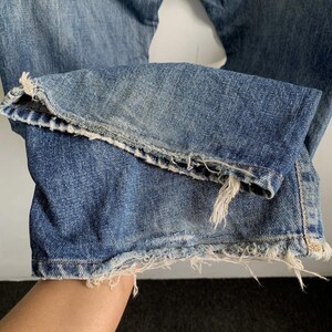 Peut inclure: Gros plan sur l'ourlet d'un jean en denim bleu. Le jean pr&eacute;sente un bord effiloch&eacute; et vieilli, avec des fils blancs visibles. Le denim montre des signes d'usure et de d&eacute;coloration, lui donnant un aspect vintage.