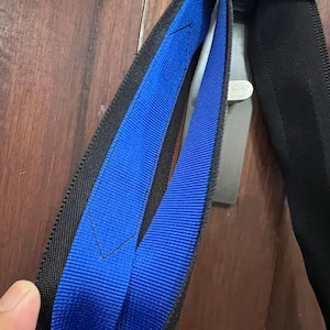 K&ouml;nnte beinhalten: Nahaufnahme eines schwarz-blauen Gurtes mit silbernem Metallverschluss. Der Gurt hat eine blaue Mitte und schwarze R&auml;nder. Der Gurt besteht aus einem gewebten Material.