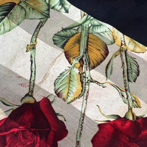 May include: A fabric with a floral pattern featuring large red roses, green leaves, and yellow accents. The roses are set against a background of diagonal gray and white stripes, with a solid black section in the corner.