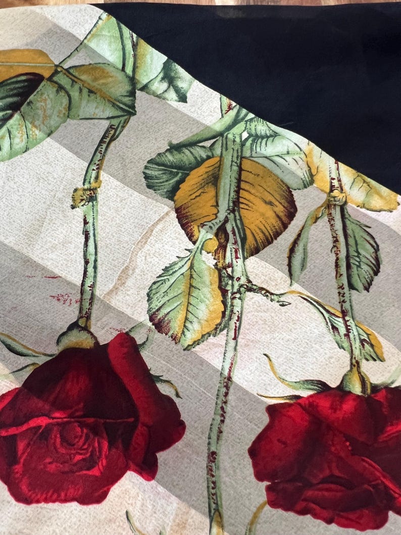 May include: A fabric with a floral pattern featuring large red roses, green leaves, and yellow accents. The roses are set against a background of diagonal gray and white stripes, with a solid black section in the corner.