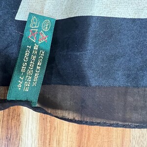 May include: A black silk scarf with a green tag. The tag has text in Korean and English, including "SILK 100%" and a phone number. The scarf has a dark blue and light grey pattern.
