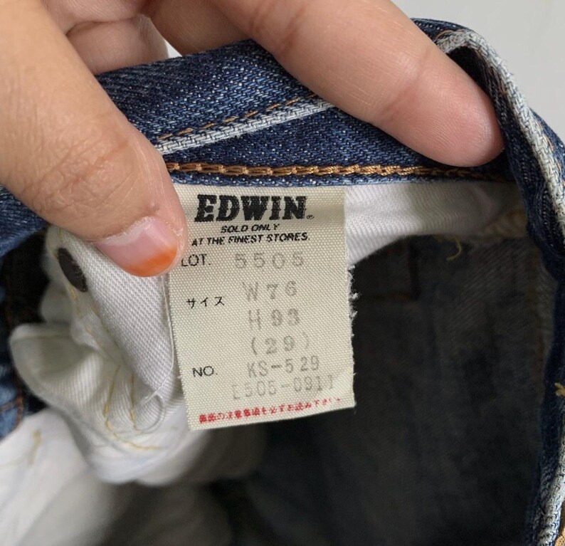 Peut inclure: Gros plan sur une &eacute;tiquette de jean bleu. L'&eacute;tiquette indique "EDWIN" et comprend des d&eacute;tails tels que "W76", "H93 (29)" et "KS-529 2505-0911". L'&eacute;tiquette est blanche avec du texte noir.