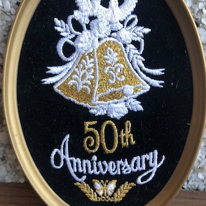 May include: A gold and white embroidered oval plaque with a bell, doves, and the text "50th Anniversary".