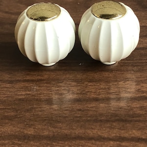 以下が含まれることがあります： 金色のトップが付いた白いセラミック製のノブが2つ。ノブはリブ模様です。