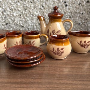 May include: A white ceramic mug with a black handle and the text "But First, Coffee" in a bold, black font. The mug is set against a blurred background, suggesting a cozy setting.