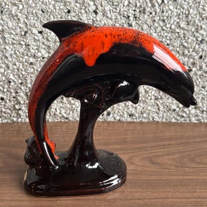 May include: A black and orange ceramic dolphin figurine. The dolphin is leaping out of the water and has a black base.