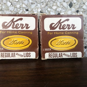 May include: Two brown boxes of Kerr Regular Mason Lids for home canning. Each box contains one dozen lids.