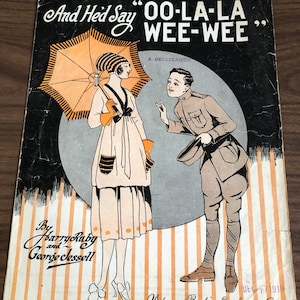May include: A vintage sheet music cover featuring a black and white illustration of a woman in a white dress holding an umbrella and a man in a military uniform. The title of the song is "And He'd Say "OO-LA-LA WEE-WEE"" by Harry Ruby and George Jessell. The cover is dated December 17, 1919.