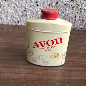 May include: A white metal tin with a red lid. The tin has a gold and black illustration of a horse-drawn carriage and the text "AVON TALC FOR MEN SPICY".