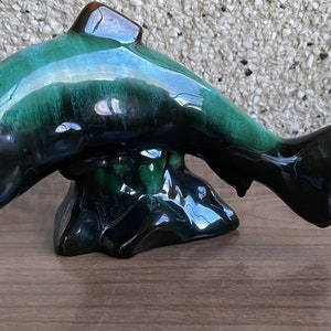 May include: A ceramic dolphin figurine with a green and black glaze. The dolphin is leaping out of the water and has a realistic design.