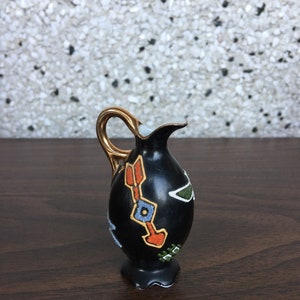 May include: A small black ceramic jug with a gold handle and a geometric design in orange, blue and green.